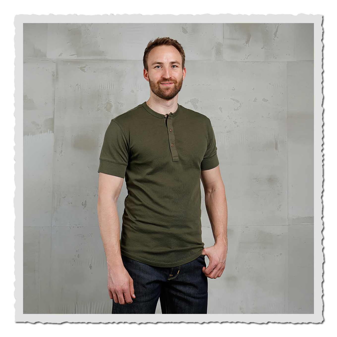Model im olivgrünen Kurzarm-Henley vor heller, leicht strukturierter Wand im Studio.